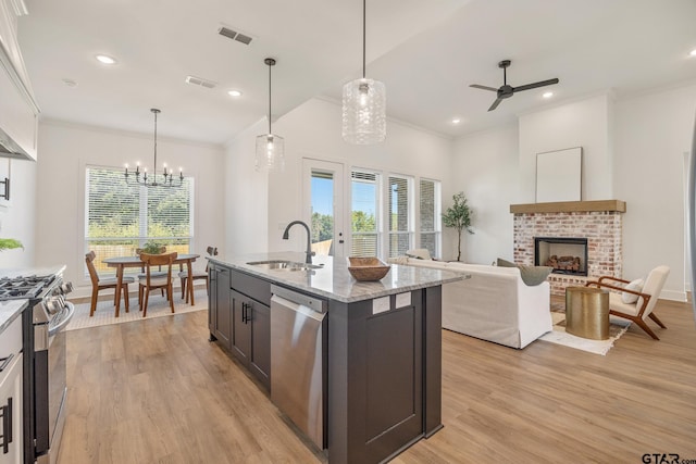 kitchen featuring sink, light stone counters, a brick fireplace, stainless steel appliances, and a kitchen island with sink