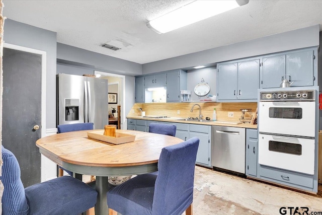 kitchen featuring blue cabinets, sink, tasteful backsplash, a textured ceiling, and appliances with stainless steel finishes