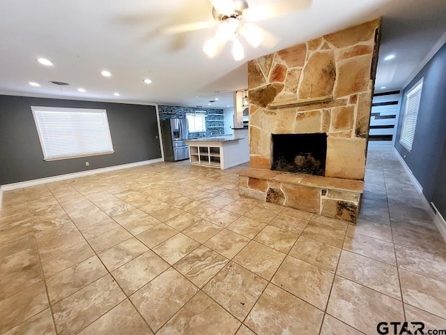 unfurnished living room featuring a stone fireplace, a wealth of natural light, and ceiling fan