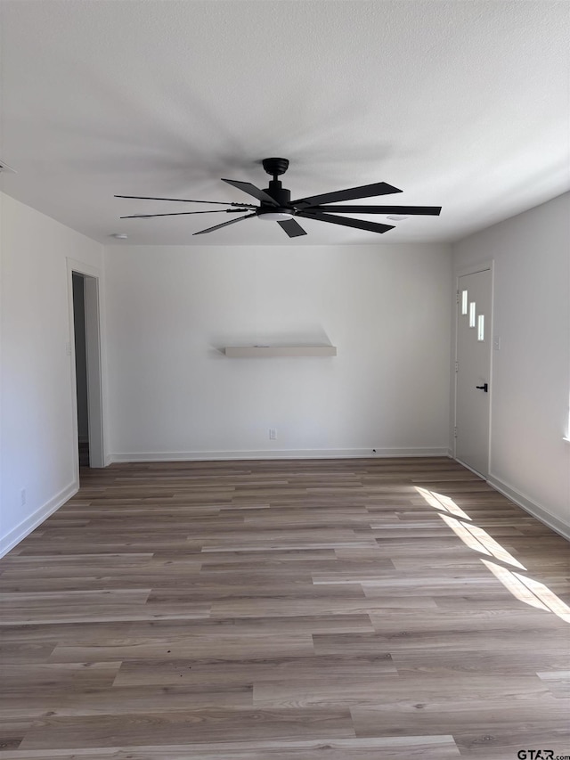 unfurnished room with ceiling fan, a textured ceiling, baseboards, and wood finished floors