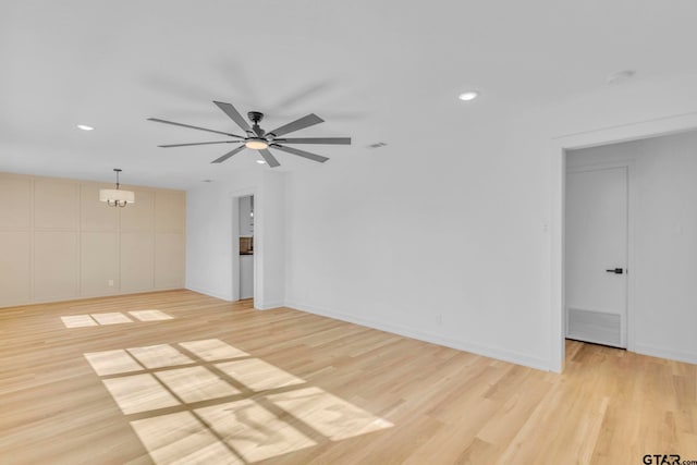 spare room with ceiling fan with notable chandelier and light hardwood / wood-style floors