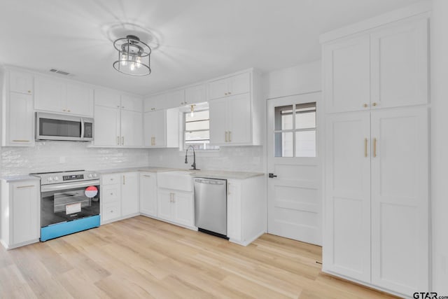 kitchen with sink, decorative backsplash, light wood-type flooring, appliances with stainless steel finishes, and white cabinetry