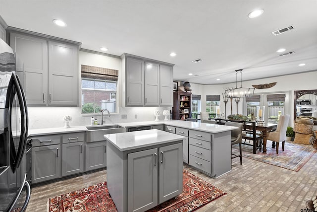 kitchen featuring a peninsula, gray cabinetry, black fridge, and a sink