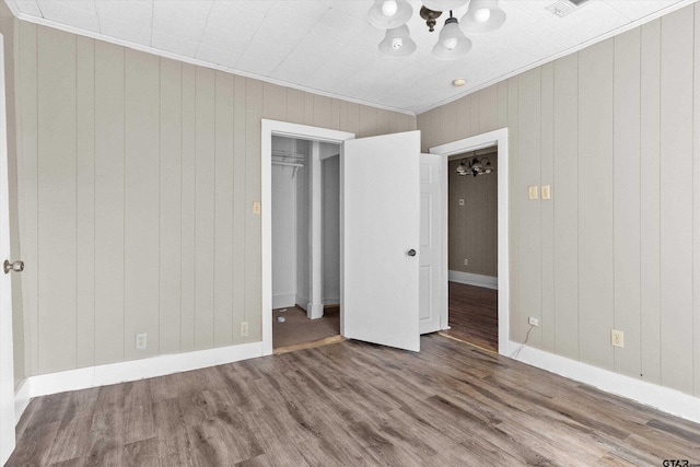 unfurnished bedroom featuring wood walls, an inviting chandelier, hardwood / wood-style flooring, and ornamental molding