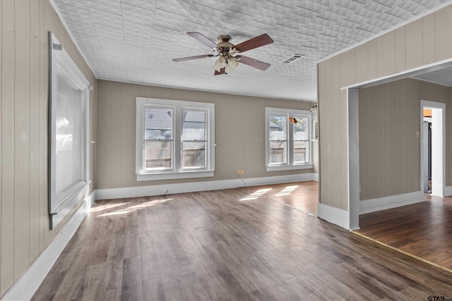 interior space featuring dark wood-type flooring, wooden walls, and ceiling fan