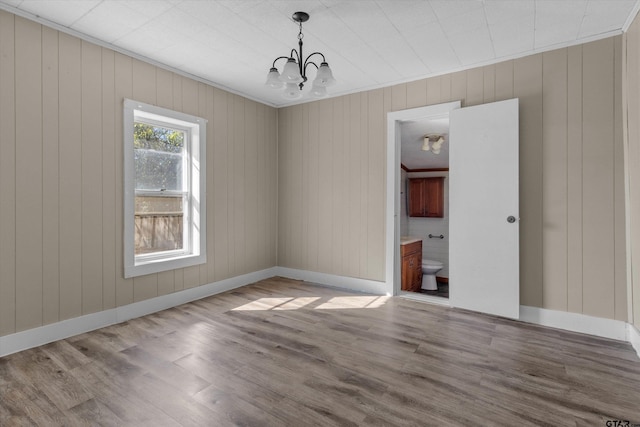 unfurnished room with hardwood / wood-style floors, a notable chandelier, and wooden walls