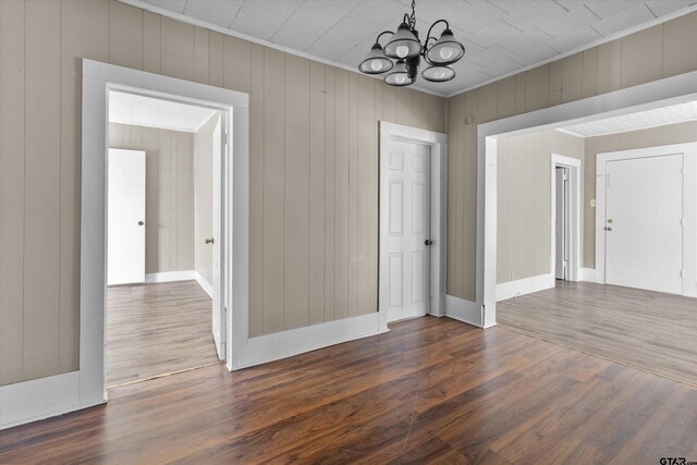 unfurnished dining area with dark wood-type flooring, wooden walls, and an inviting chandelier