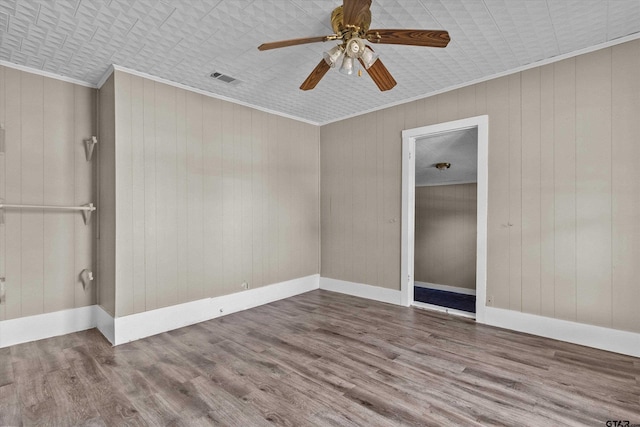 spare room featuring crown molding, wooden walls, hardwood / wood-style flooring, and ceiling fan