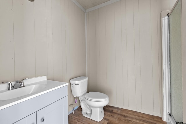 bathroom with wood-type flooring, crown molding, vanity, wood walls, and toilet