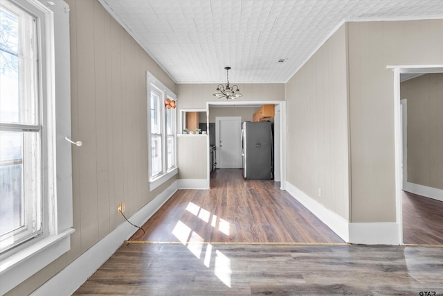 unfurnished dining area with dark wood-type flooring, wooden walls, and a notable chandelier