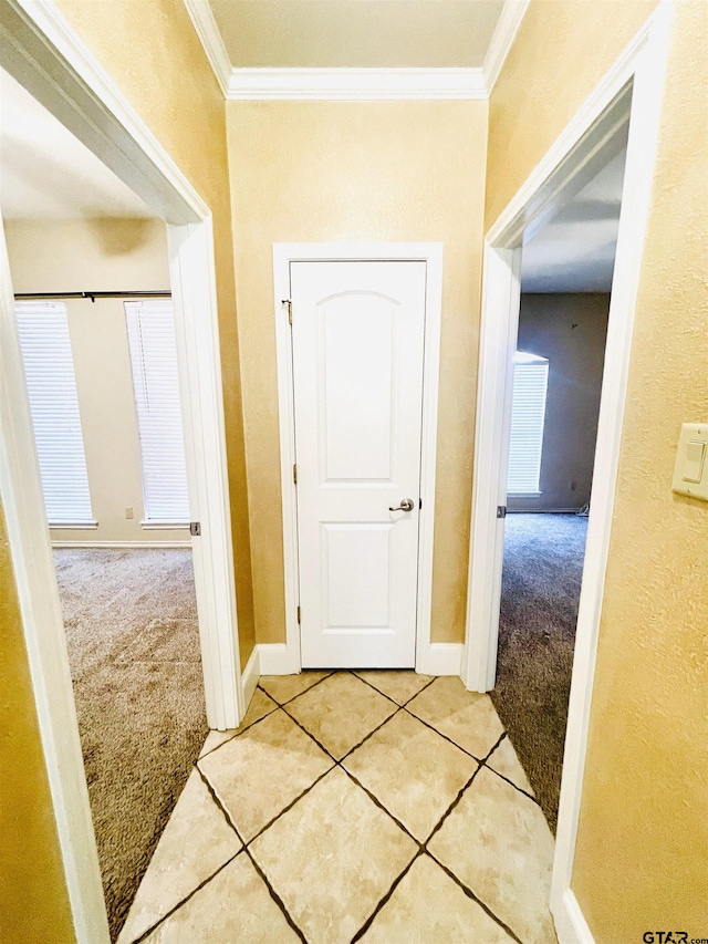 hall featuring baseboards, carpet floors, tile patterned flooring, and crown molding