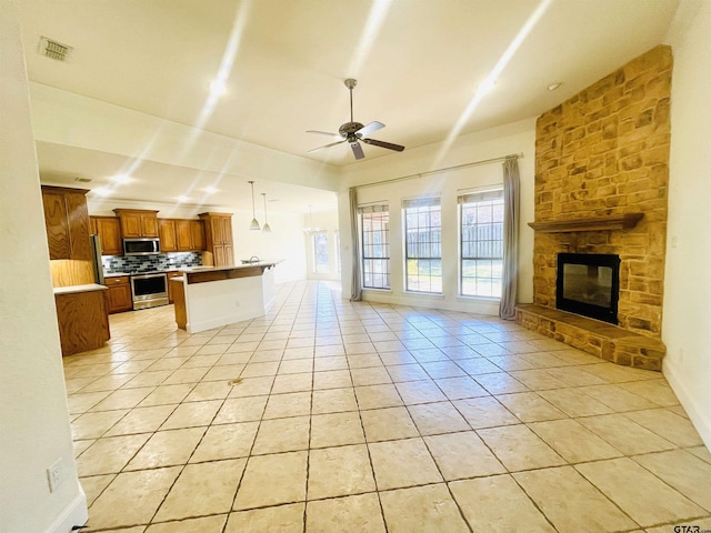 living room featuring light tile patterned floors, a stone fireplace, visible vents, and a ceiling fan