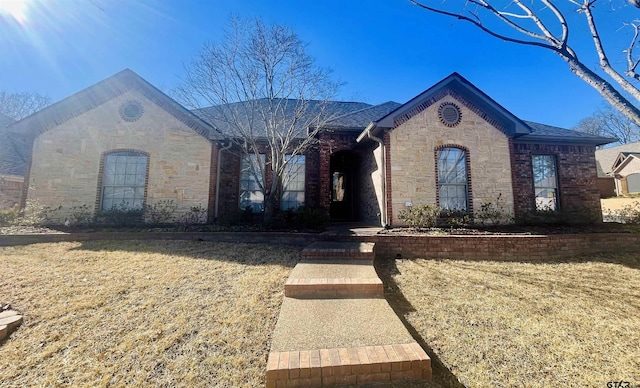 french country style house with stone siding, brick siding, and a front yard