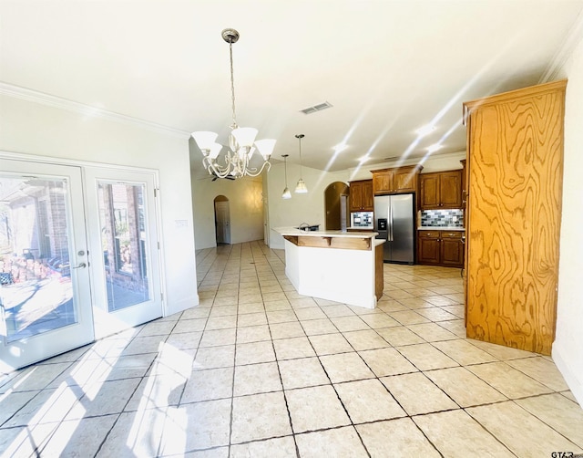 kitchen featuring a center island with sink, arched walkways, stainless steel fridge with ice dispenser, decorative light fixtures, and light countertops