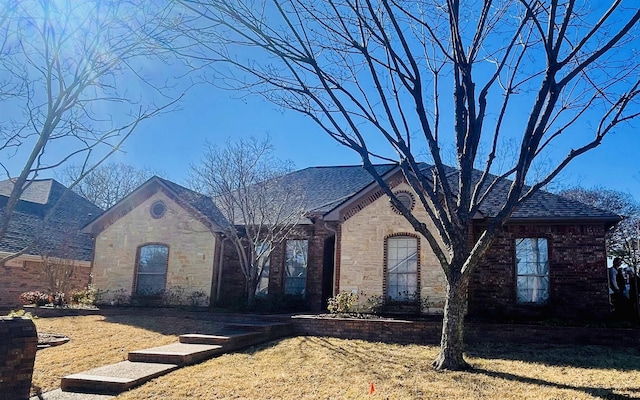 french country home with stone siding, a front lawn, and brick siding