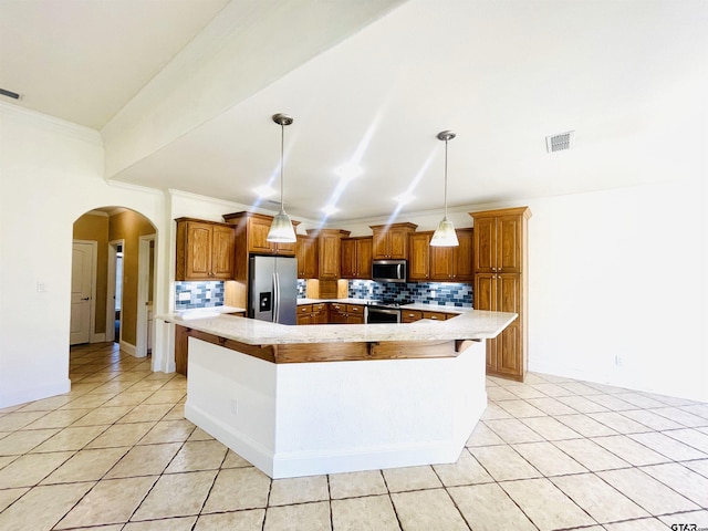 kitchen featuring arched walkways, brown cabinets, a spacious island, hanging light fixtures, and appliances with stainless steel finishes