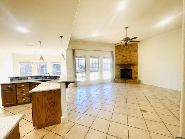 kitchen with a breakfast bar, hanging light fixtures, open floor plan, a sink, and a stone fireplace