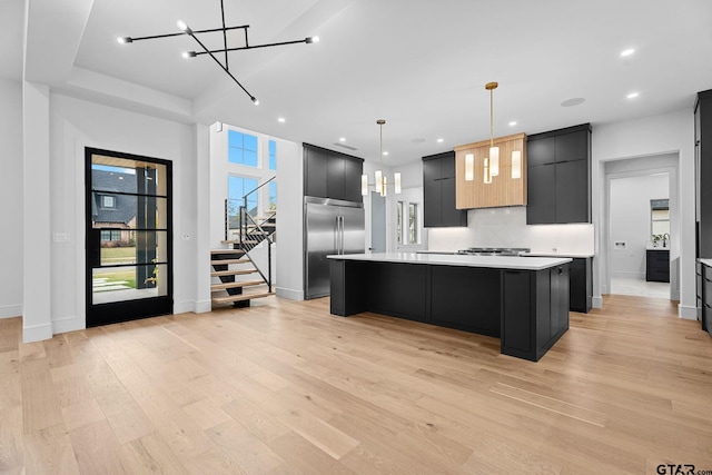 kitchen with built in refrigerator, a kitchen island, hanging light fixtures, and light hardwood / wood-style floors