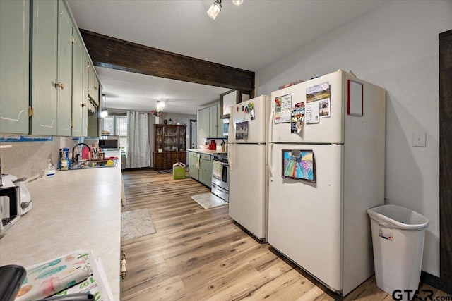 kitchen featuring a sink, light countertops, freestanding refrigerator, stainless steel range with gas cooktop, and green cabinets