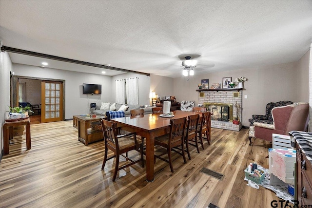 dining space featuring light wood-style floors, ceiling fan, a fireplace, a textured ceiling, and visible vents