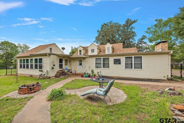 back of property with a yard, an outdoor fire pit, a chimney, fence, and a patio