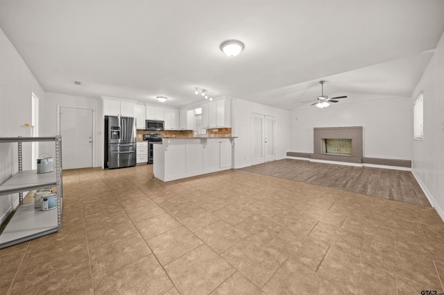 kitchen with vaulted ceiling, a fireplace, decorative backsplash, white cabinetry, and stainless steel appliances