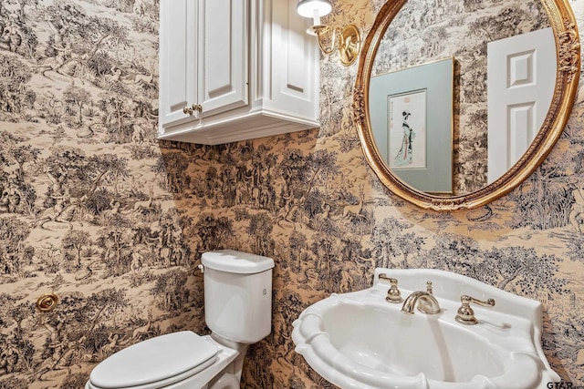 bathroom featuring toilet, wallpapered walls, and a sink