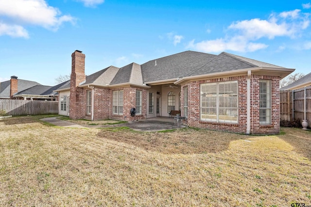 rear view of house with brick siding, a patio area, a yard, and fence