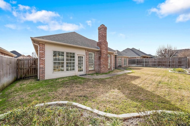 rear view of property featuring a fenced backyard, a yard, a shingled roof, brick siding, and a chimney