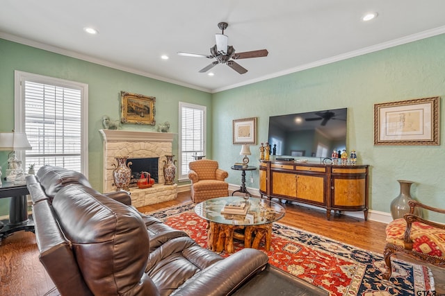 living area featuring a stone fireplace, crown molding, ceiling fan, and wood finished floors