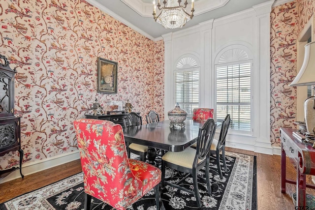 dining space featuring wood finished floors, baseboards, wallpapered walls, crown molding, and a notable chandelier