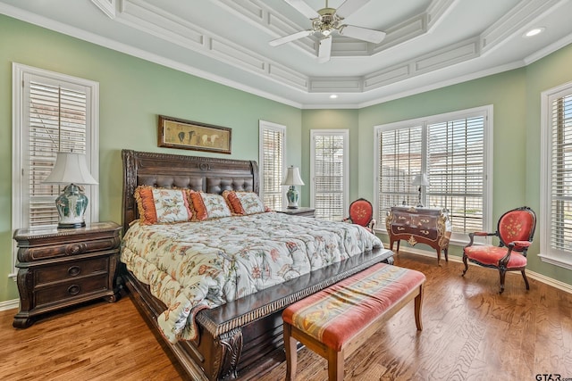 bedroom featuring baseboards, ornamental molding, light wood-style flooring, a raised ceiling, and a ceiling fan