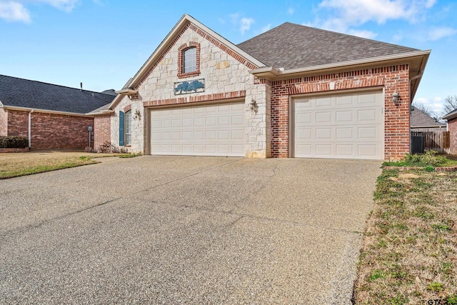 french country inspired facade with driveway, stone siding, a shingled roof, a garage, and brick siding