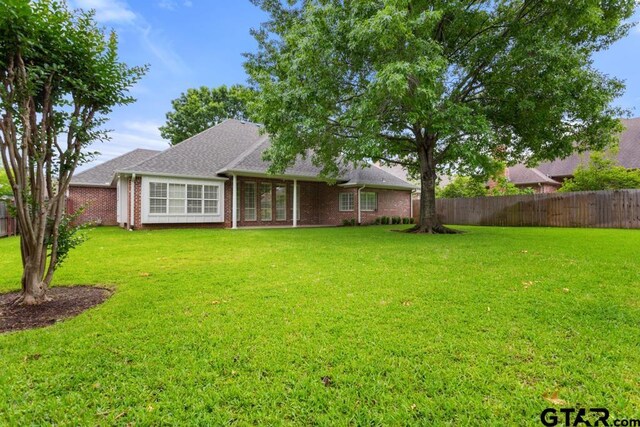 6529 Salisbury Ln, Tyler, TX 75703 - rear view of house featuring brick siding, a fenced backyard, a shingled roof, and a yard