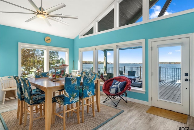 dining area with a water view, ceiling fan, high vaulted ceiling, light wood-style flooring, and baseboards