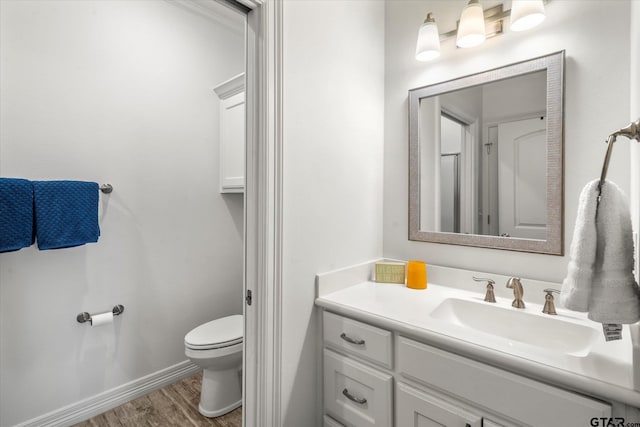 bathroom featuring baseboards, wood finished floors, toilet, and vanity