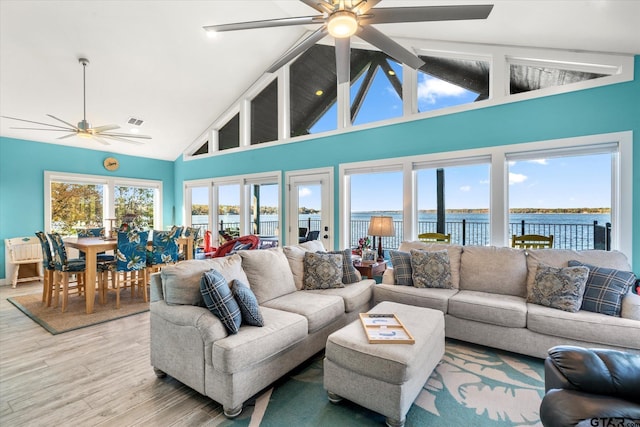 living area with a water view, ceiling fan, light wood-style flooring, and high vaulted ceiling