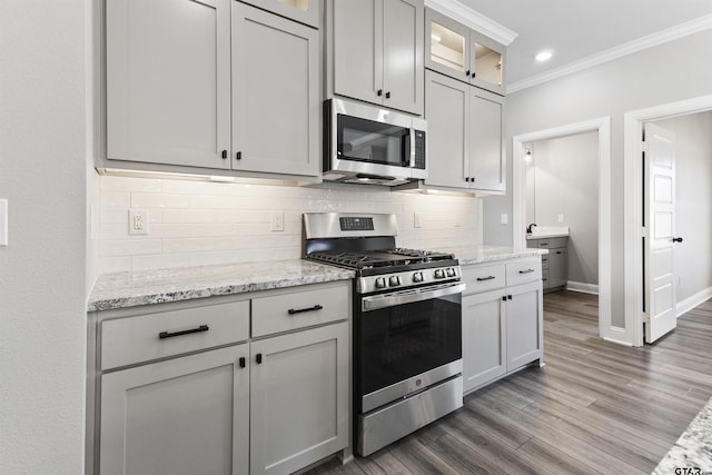 kitchen with backsplash, hardwood / wood-style floors, crown molding, stainless steel appliances, and light stone counters