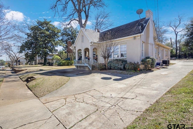 view of property exterior with brick siding, driveway, and a chimney