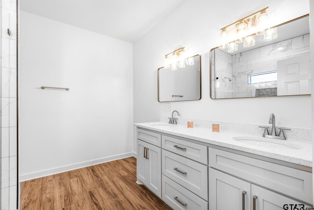 bathroom with tiled shower, wood finished floors, baseboards, and a sink