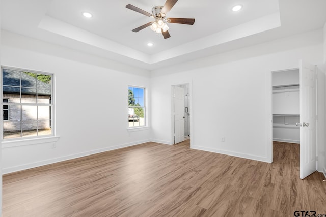 unfurnished bedroom featuring light wood finished floors, a raised ceiling, and baseboards