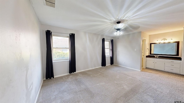 unfurnished bedroom with ceiling fan, light colored carpet, connected bathroom, and multiple windows