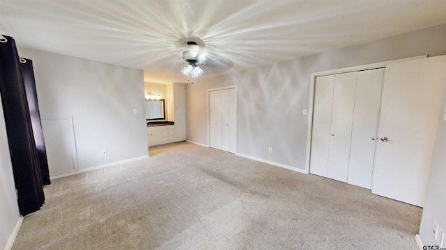 unfurnished bedroom with two closets, light colored carpet, ceiling fan, and ensuite bathroom