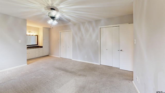 unfurnished bedroom with light carpet, two closets, and ceiling fan