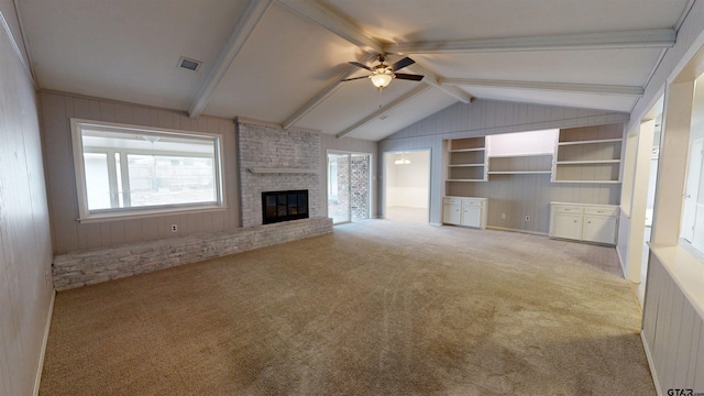 unfurnished living room with vaulted ceiling with beams, a brick fireplace, wooden walls, carpet flooring, and ceiling fan