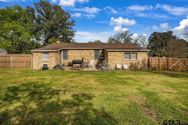 back of house featuring a fenced backyard, brick siding, and a lawn