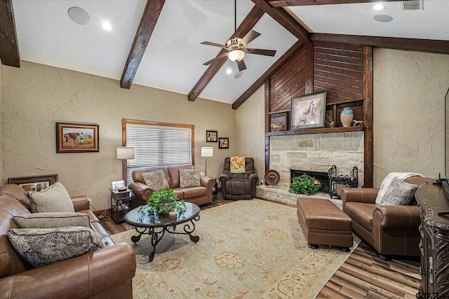 living room with hardwood / wood-style floors, vaulted ceiling with beams, ceiling fan, and a stone fireplace