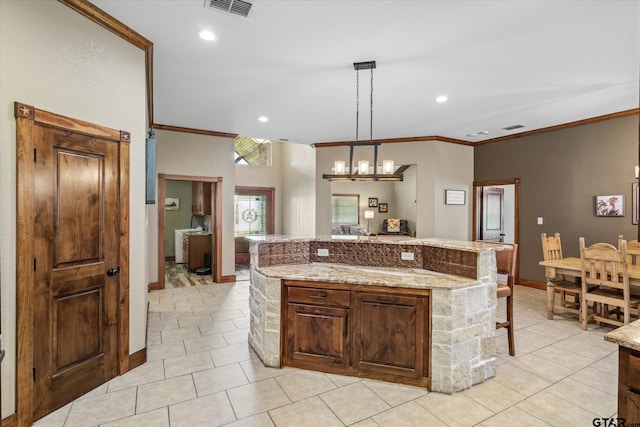 kitchen with light stone countertops, ornamental molding, light tile patterned floors, a kitchen island, and hanging light fixtures