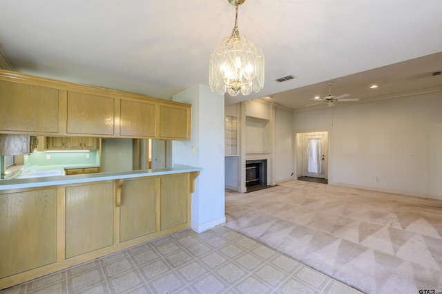 kitchen with light brown cabinets, kitchen peninsula, pendant lighting, light colored carpet, and ceiling fan with notable chandelier