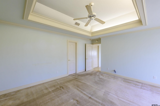 empty room with a raised ceiling, light carpet, crown molding, and ceiling fan